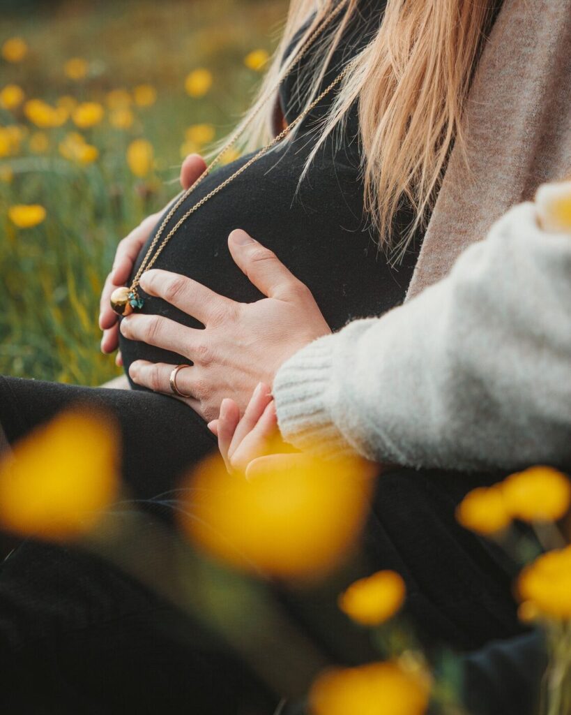 Ventre de femme enceinte entouré de fleurs jaunes, photographe grossesse dans le canton de Vaud